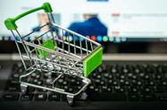 Miniature shopping cart placed on a laptop keyboard, symbolizing online shopping.