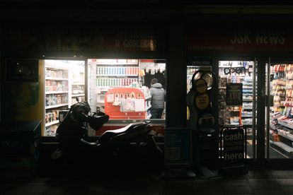 A dimly lit convenience store in London at night with a motorbike parked outside.